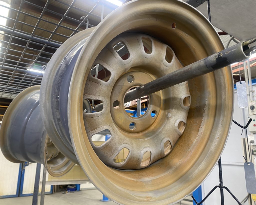 a sand blasted wheel ready to be powder coated, hangin in the factory before the booth. The wheel has had it's rust removed for premium service and finish