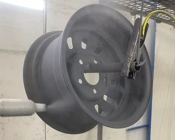 the action of powder coating a car wheel rim a sophisticated matte black. It is hanging in the both ant the powder coater is working hard for the best results